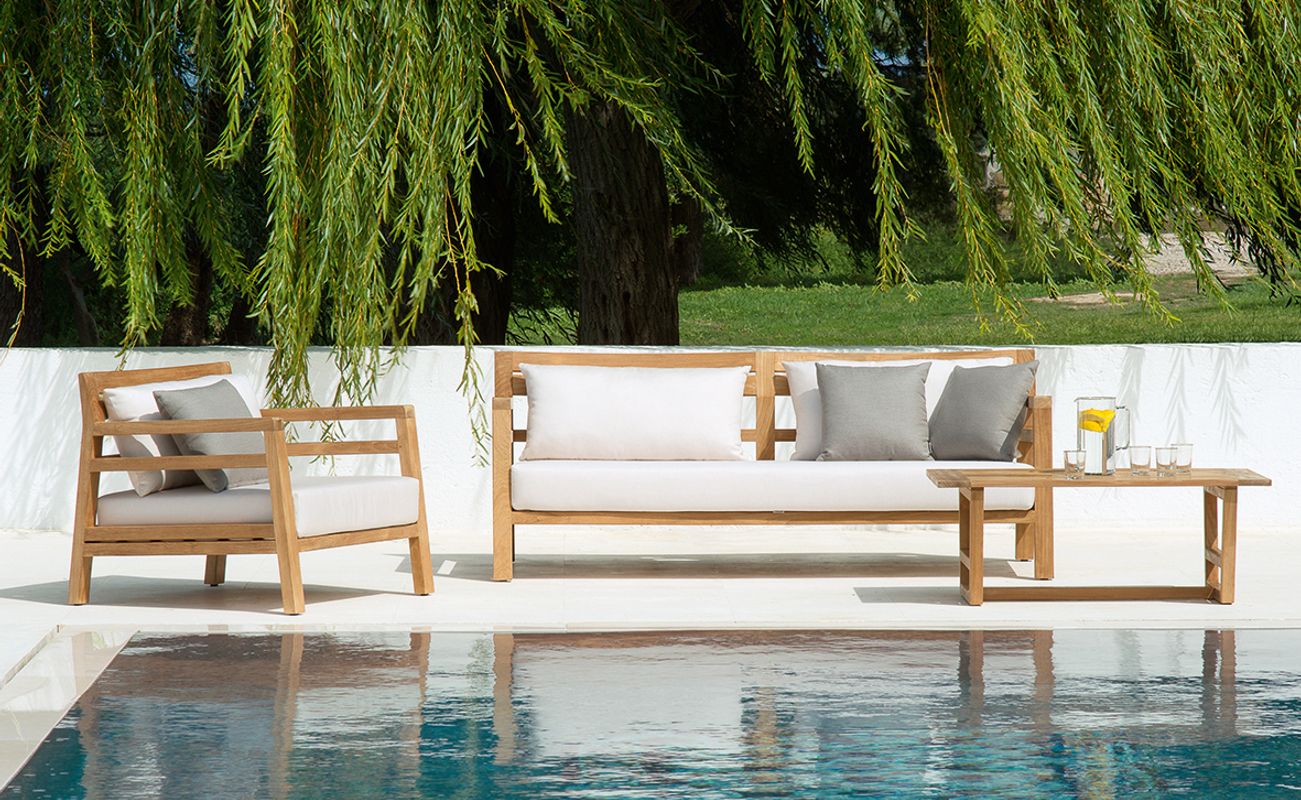 Holzmöbel im Freien, bestehend aus einer Couch, einem Sessel und einem Tisch, neben einem Pool mit klarem Wasser und einem Weidenbaum im Hintergrund.